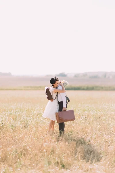 Os recém-casados vestidos vintage estão abraçando no campo ensolarado. A vista lateral vertical — Fotografia de Stock