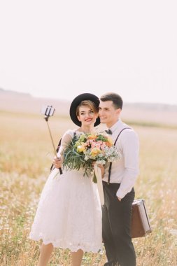 Vintage giyinmiş yeni evliler görünümünü güneşli alan arka plan selfiestick kullanarak selfie alıyor.
