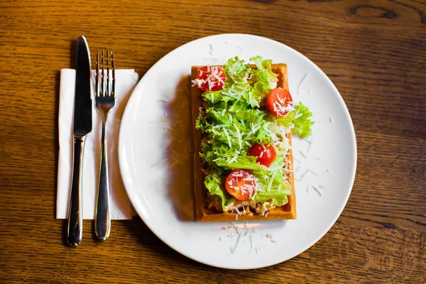 De samenstelling van de Belgische wafels met salat, tomaten, kaas en othe groenten op de houten tafel geplaatst. Close-up boven de foto's voor de tabel instellen. — Stockfoto