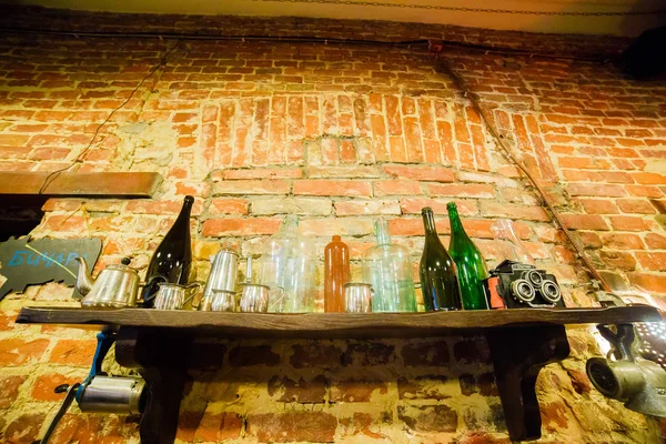 The upside view of the wooden shelf with the glass bottles and antique camera hanging on the brick wall of the cafe. — Stock Photo, Image