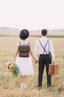 Vaktinizi güneşli alanında yeni evliler arka tarafında dikey görünüm. Adam ahşap çanta taşıyor ise gelin renkli buket tutuyor.