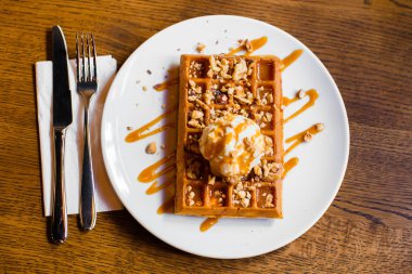 Masayı hazırla. Beyaz dondurma ile Belçika waffle lezzetli bileşimi karamel ve fındık ile dekore edilmiş.