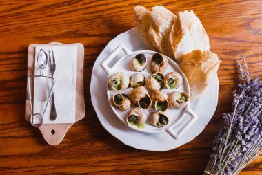 Salyangoz kabukları ve kuru mor çiçekler ve çatal bıçak takımı çevrili ekmek yiyecek bileşimi. Görünümünün üst.