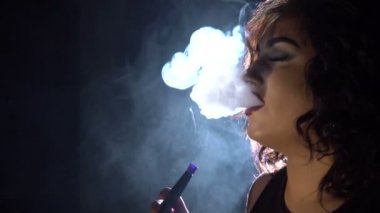Güzel bir kadın dışarı kalın nargile duman üfleme olduğunu. Yakın çekim yan portre. Karanlık bir odada konum.
