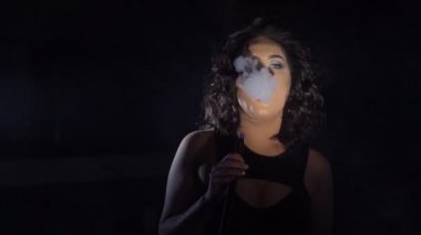 Yatay glamour portre. Siyah saçlı kadın tarafından nargile sigara ve siyah stüdyo kalın duman üreten chilling.