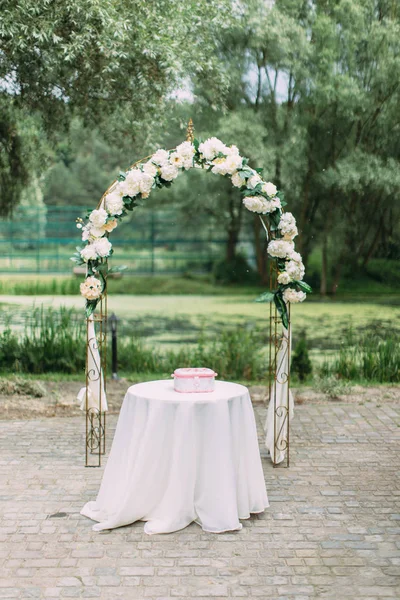 Full-length view of the arch with white flowers placed behind the table with little pink box on it. — Stock Photo, Image
