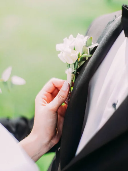 La vista de cerca de las manos novias tocando el boutonniere en el traje del novio . — Foto de Stock