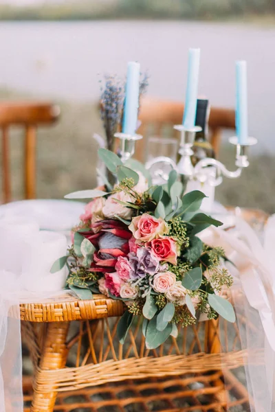 O buquê de casamento das rosas coloridas colocadas na mesa tecida com castiçais. Localização da praia . — Fotografia de Stock