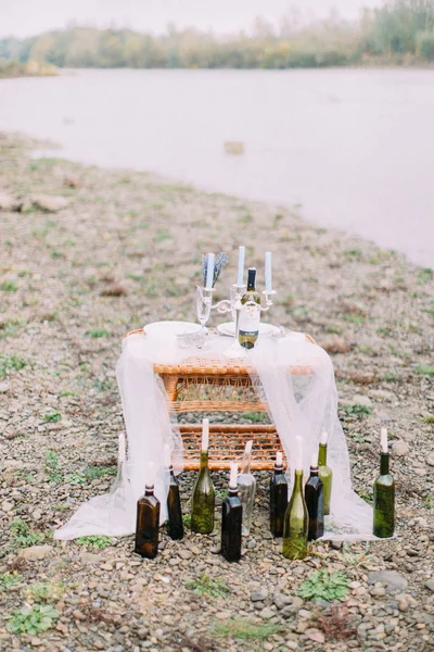 Çok güzel wickered tablo ile mumlar ve şarap şişeleri sahilde şeklinde mum tribünde civarında.