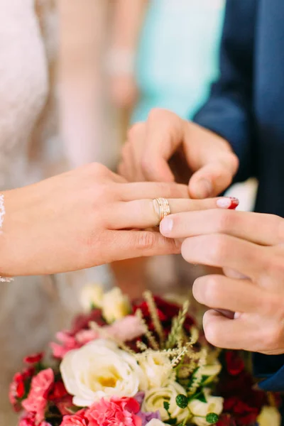 Руки жениха надевают обручальное кольцо на палец невесты под свадебный букет . — стоковое фото