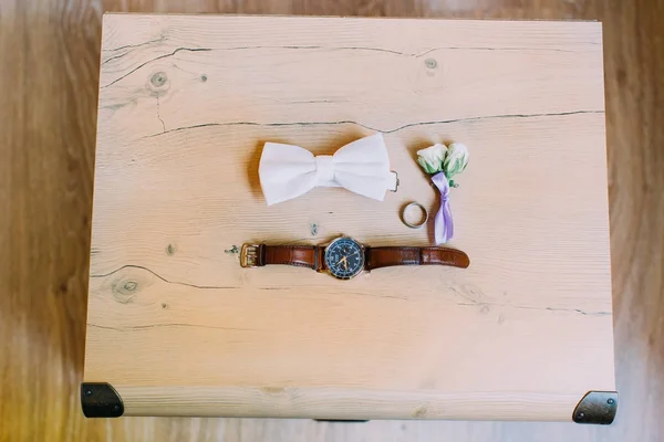 El complemento de la boda que consiste en corbata de lazo blanco, anillo, reloj de mano y boutonniere pequeña rosa . — Foto de Stock