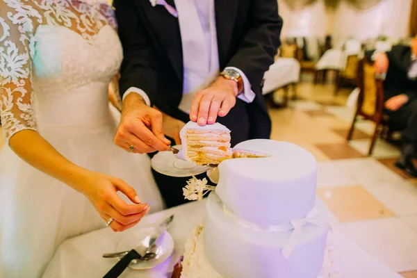Hände des Bräutigams legen das erste Stück der Hochzeitstorte auf den Teller. — Stockfoto