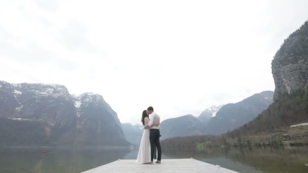 De full-length horizontale weergave van het verliefde mooie paar knuffelen en zoenen op de piere onder Bergen. De panorama-weergave. — Stockvideo