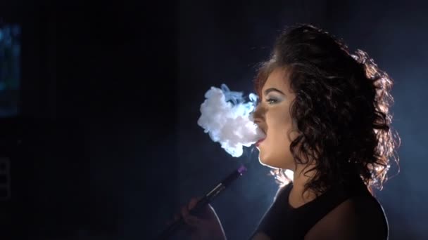 Catching woman is having the rest by smoking the hookah. The side view of the blowing out the thick smoke in the dark studio. — Stock Video