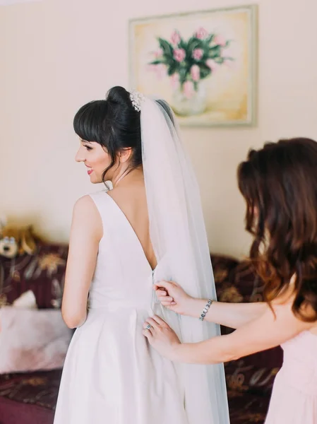 La dama de honor está ayudando a la novia con el vestido de novia. Vista trasera . —  Fotos de Stock
