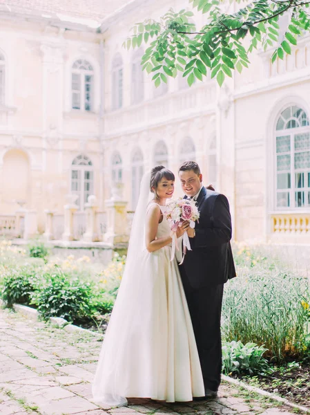 Photo pleine longueur des jeunes mariés heureux tenant le bouquet de mariage dans la rue . — Photo