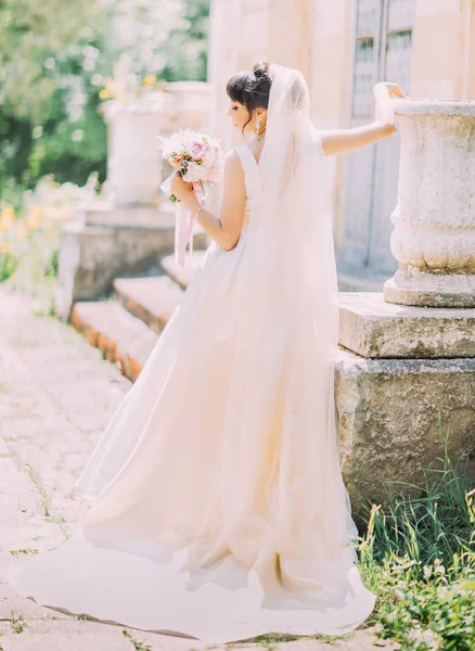 A visão traseira da noiva bonita com o buquê de casamento perto do edifício velho . — Fotografia de Stock