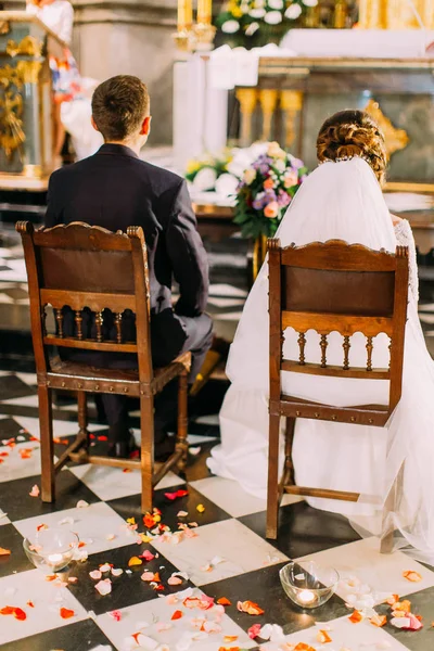 Вид ззаду молодих, що сидять на стільцях під час весільної церемонії в церкві . — стокове фото