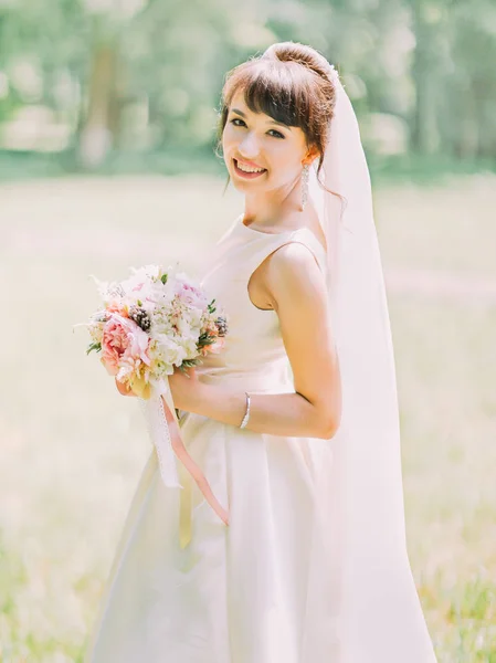 Retrato de meio comprimento lateral da bela noiva sorridente segurando o buquê de casamento de peônias . — Fotografia de Stock