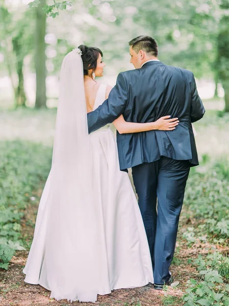 Visão traseira completa dos recém-casados felizes andando ao longo da floresta . — Fotografia de Stock