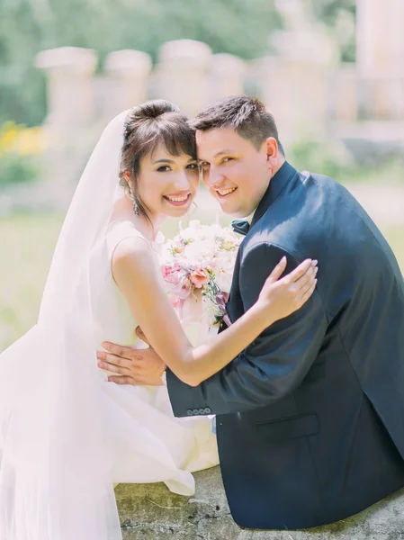 Känslomässiga porträtt av de krama nygifta sitter på fontänen. Bakifrån. — Stockfoto
