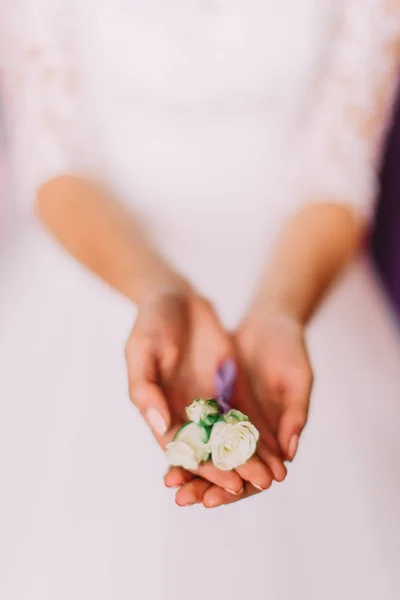 Brides hands are holding the little boutonniere of white roses. — Stock Photo, Image
