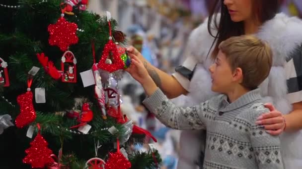 La mamma felice e il suo figlioletto stanno osservando le decorazioni sull'albero di Natale nel centro commerciale. Vista laterale da vicino . — Video Stock