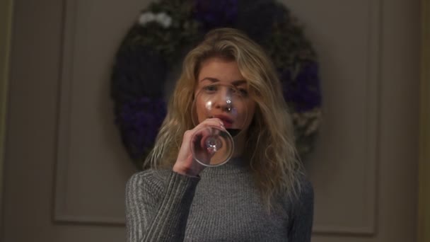 Horizontale weergave van het mooie blonde meisje het drinken van wijn op de achtergrond van de kroon van Kerstmis. — Stockvideo