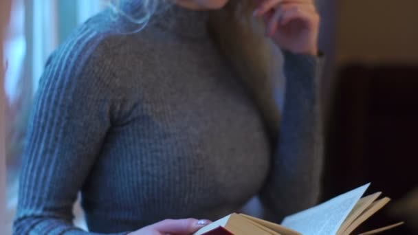 Rörliga närbild av attraktiva flickan bär glasögon och läsa bok nära fönstret. — Stockvideo
