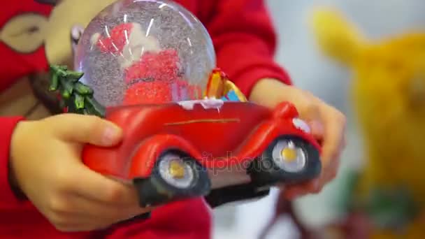 Les mains du petit garçon serrent la boule de neige sous la forme de la voiture. Temps de Noël . — Video