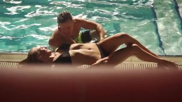 Молодая пара плавает в бассейне в роскошном азиатском отеле, весело провести время и поговорить. Мужчина смотрит на девушку и говорит ей что-то. Блондинка лежит на краю бассейна . — стоковое видео