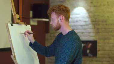 Kızıl saçlı sanatçı bir resim çizim ve bir şeyler anlatıyor