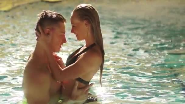 Seksi genç çift lüks otel havuzunda kalıyor. Onların yüzleri birbirine bakarak ve öpüşme çok yakın. Onlar gülümseyen ve sarılma. Kadın şefkatle elini tutan vücut mans — Stok video