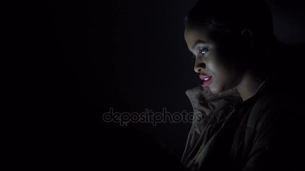Czarna kobieta czyta coś w jej iphone stojący w ciemności — Wideo stockowe