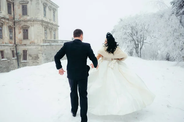 Close-up back view of the bride running away from groom along the path covered with fluffy snow. — Stok Foto