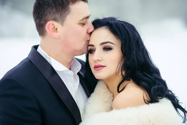 Ritratto orizzontale dello sposo che bacia la bella sposa bruna seria sulla fronte. Orario invernale . — Foto Stock