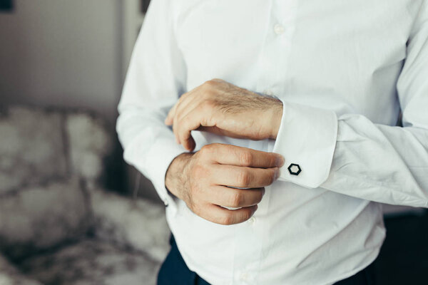 Wedding preparation of the groom. Hands are buttoning the clifflinks on the shirt.