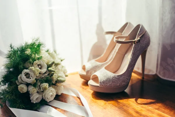 Közeli kép oldalnézetből a esküvői csokor fehér rózsát helyezett közelében a bézs színű esküvői magas sarkú az ablak mellett. — Stock Fotó