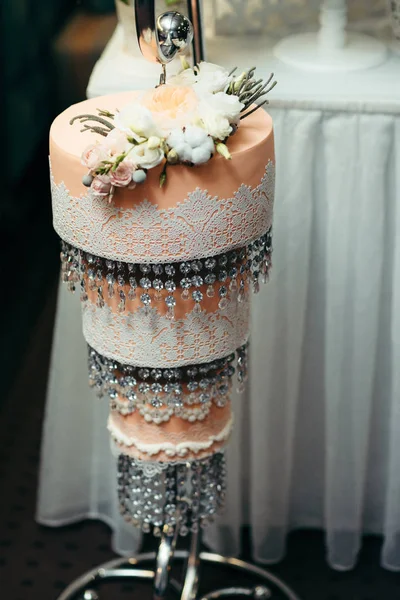 Трехэтажный оранжевый свадебный торт украшенный белыми и бежевыми розами и висячими бусами . — стоковое фото