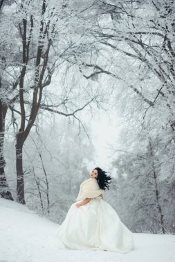 Uzun güzel siyah saçlı ayakta ormandaki karlı yolda büyüleyici gelinle tam uzunlukta görünümünü.