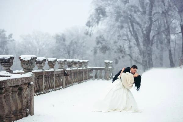 Full-length shot of the beautiful happy newlyweds dancing on the snowy path. — Stock Photo, Image