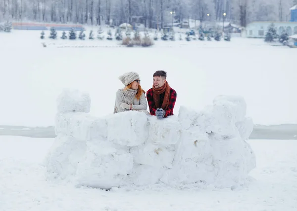 Full-length view of the cheerful couple standing behind the snow wall and laughing. Winter village location. — Stock Photo, Image