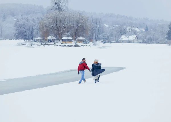 A vista horizontal para trás de dois amantes de mãos dadas enquanto caminham ao longo do campo nevado. Ambiente de Natal . — Fotografia de Stock