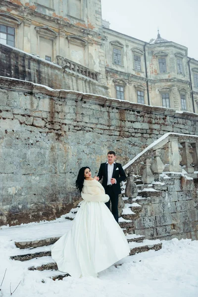 Vewrical de cuerpo entero de la encantadora pareja alegre recién casada de pie en el starsif del viejo edificio cubierto de nieve . — Foto de Stock