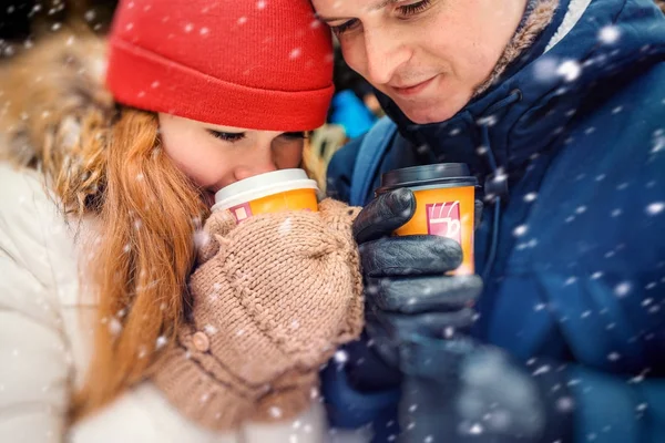 Γκρο πλαν οριζόντια πορτρέτο του το ελκυστικό νεαρό ζευγάρι πίνει καφέ και το τσάι στη διάρκεια της χιονόπτωσης αφράτο. — Φωτογραφία Αρχείου