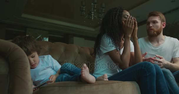 Família multirracial está tendo o conflito, enquanto o filho pequeno está jogando no telefone celular e deitado no sofá. Mãe afro-americana emocional . — Vídeo de Stock