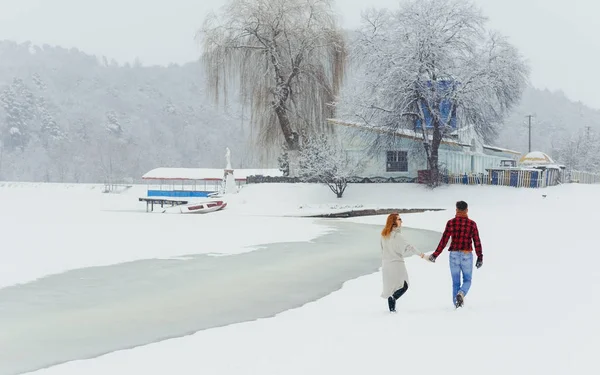 Visão traseira do casal feliz de mãos dadas durante sua caminhada ao longo da paisagem nevada. Tempo de Natal . — Fotografia de Stock