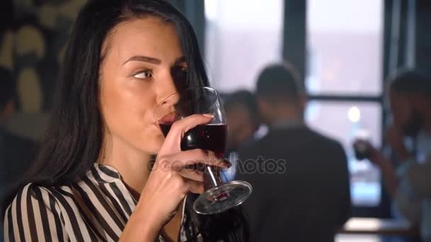 La foto de cerca de la mujer con el pelo largo y negro bebiendo cerveza oscura y ordenando su cabello en el fondo borroso de sus amigos en el café . — Vídeos de Stock