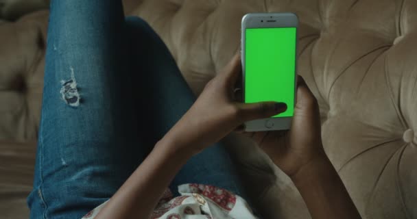 De Afro-Amerikaanse vrouw is ontspannen en chatten met de GSM met groen scherm liggend op de Bank. Close-up beeld van de handen. — Stockvideo