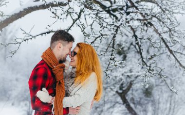 Güzel portre sevimli gülümseyen çiftin sarılma ve burun kış ormanda kar yağışı tadını çıkarırken dokunmadan.